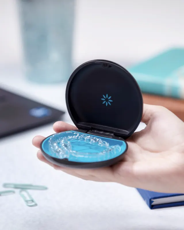 Estuche negro de Invisalign abierto en la mano, con un alineador adentro