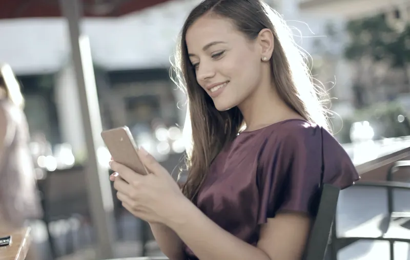 Mujer sonriendo mientras escribe en su celular