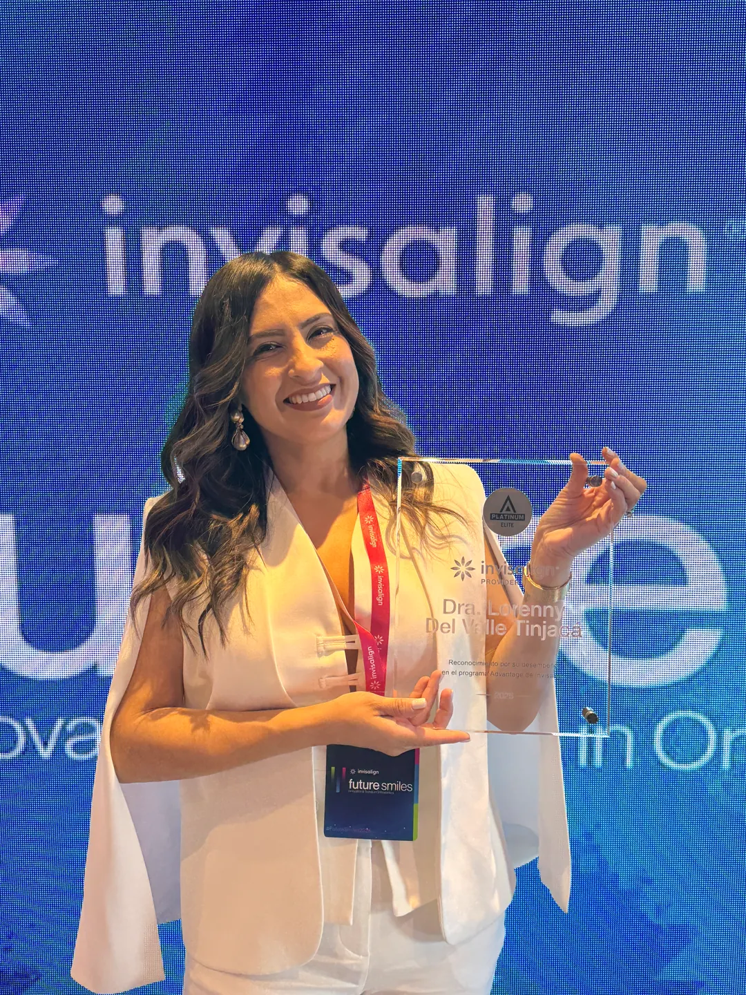 La Dra. Lorenny levantando su placa de Invisalign, con el logo de Invisalign detrás